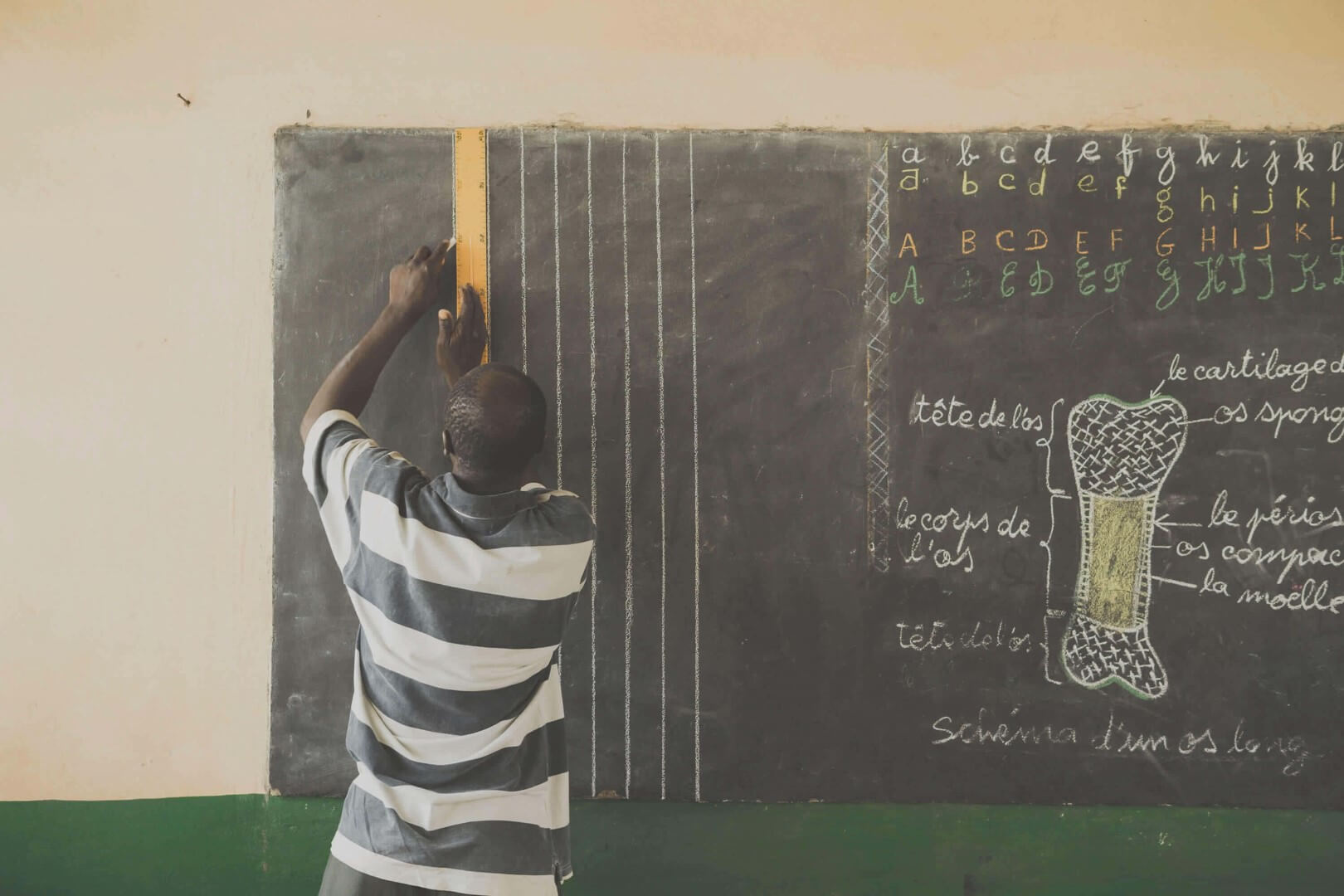Ugandan Teacher drawing lines on a blackboard.